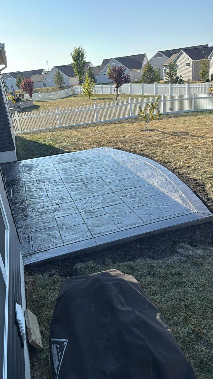 Charcoal stamped concrete patio in a white-fenced backyard
