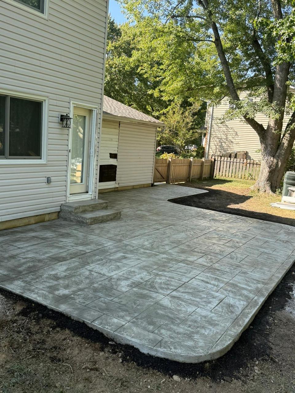 Grey stamped concrete patio with curved edge in a fenced backyard