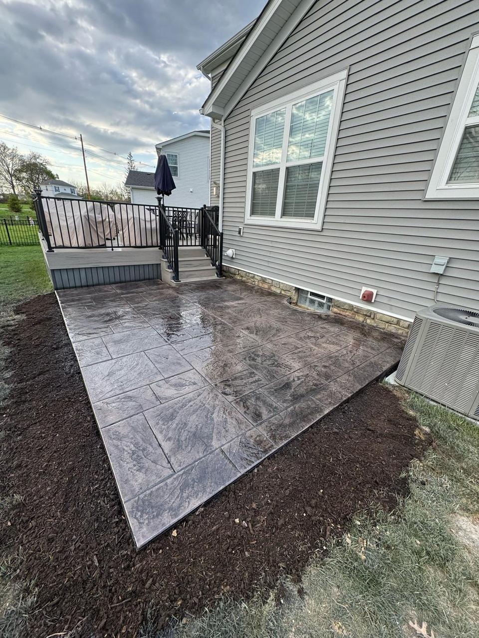 Slate stamped concrete patio beside a raised deck