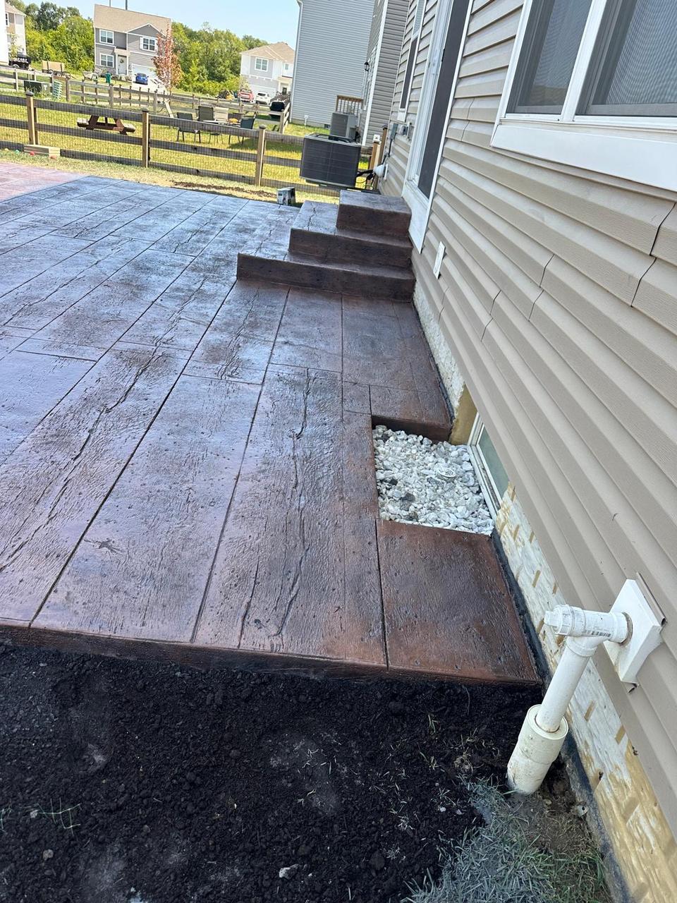 Wood plank stamped concrete patio wrapping a basement window well